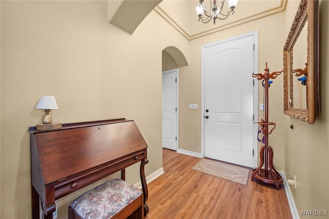 foyer featuring light wood-type flooring, arched walkways, baseboards, and a chandelier