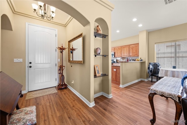 entrance foyer featuring baseboards, light wood-style flooring, recessed lighting, arched walkways, and a chandelier