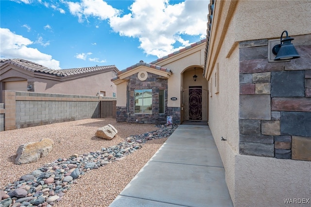 doorway to property featuring stucco siding, stone siding, a tile roof, and fence