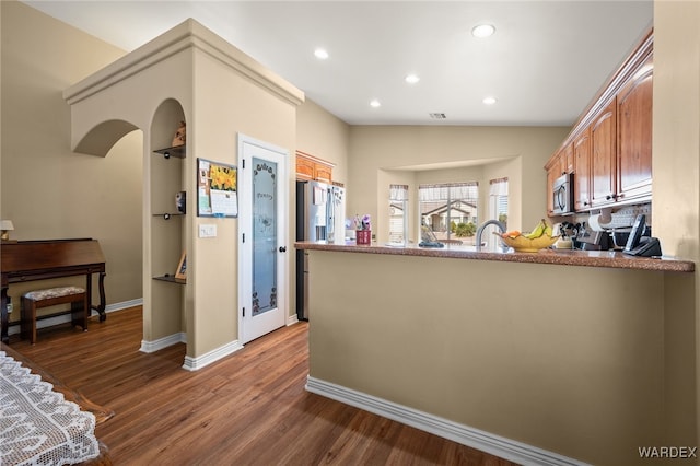 kitchen with wood finished floors, recessed lighting, stainless steel appliances, a peninsula, and vaulted ceiling