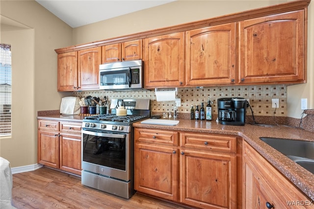 kitchen featuring light wood-type flooring, brown cabinetry, tasteful backsplash, and stainless steel appliances