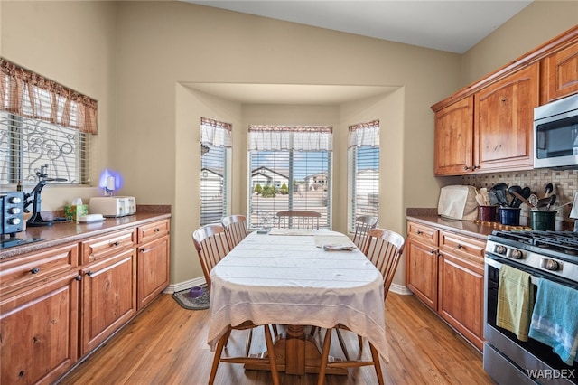 kitchen with brown cabinetry, light wood-style flooring, appliances with stainless steel finishes, and backsplash