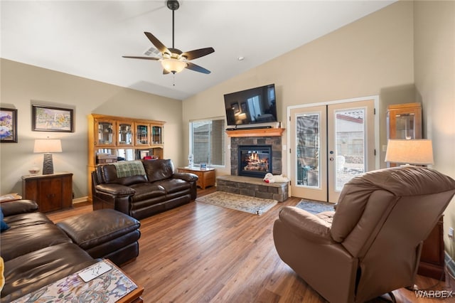 living room featuring ceiling fan, vaulted ceiling, a stone fireplace, french doors, and wood finished floors