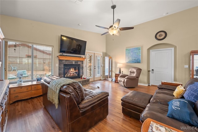 living room featuring a ceiling fan, wood finished floors, baseboards, high vaulted ceiling, and a fireplace