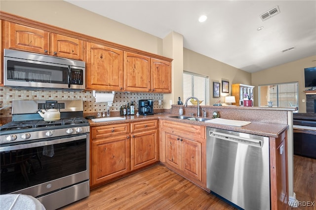 kitchen featuring visible vents, a sink, stainless steel appliances, a peninsula, and decorative backsplash