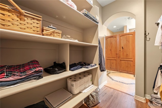 walk in closet with visible vents, arched walkways, and light wood-style flooring