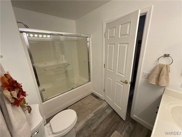 bathroom with toilet, shower / bath combination with glass door, wood finished floors, vanity, and baseboards