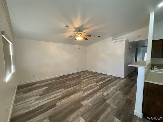 unfurnished living room with baseboards, visible vents, a ceiling fan, dark wood finished floors, and a sink