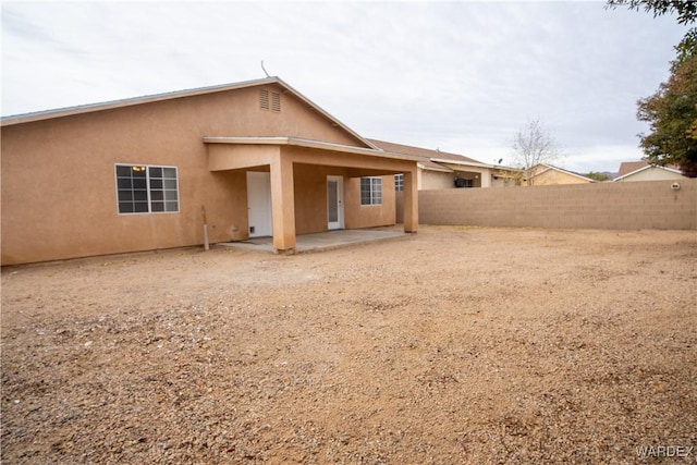 rear view of house with a patio, fence, and stucco siding