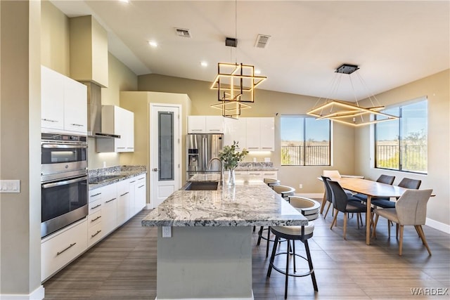 kitchen featuring appliances with stainless steel finishes, a kitchen island with sink, pendant lighting, and white cabinets