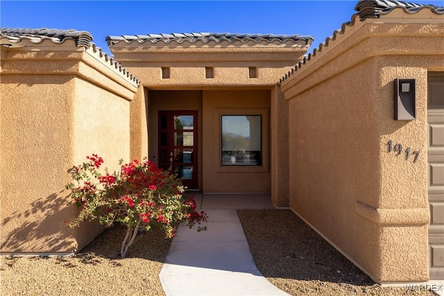 view of exterior entry with a tile roof and stucco siding