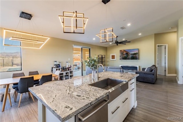 kitchen with white cabinets, an island with sink, open floor plan, a sink, and stainless steel dishwasher