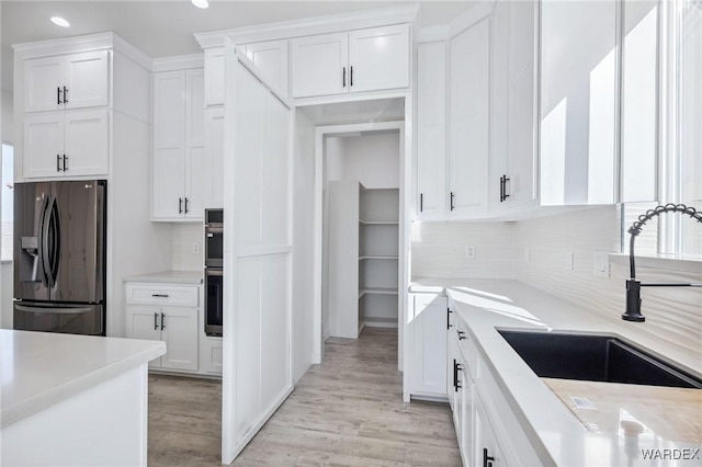 kitchen with light wood finished floors, white cabinets, stainless steel appliances, light countertops, and a sink