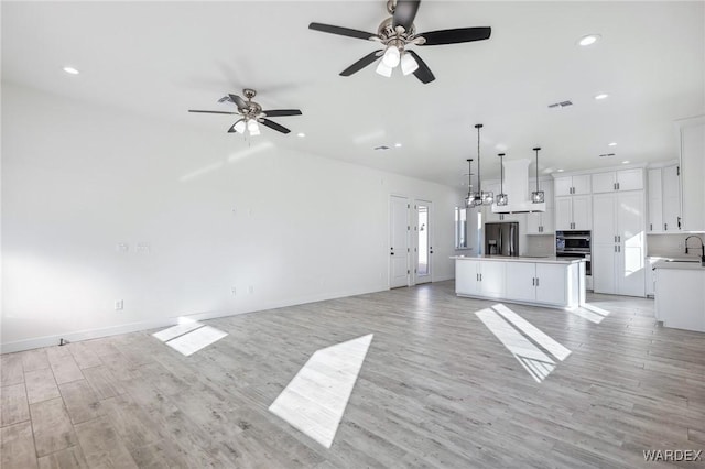 unfurnished living room with visible vents, a ceiling fan, light wood-style flooring, a sink, and recessed lighting