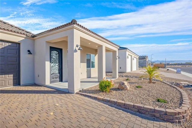 view of exterior entry with an attached garage, a tile roof, and stucco siding