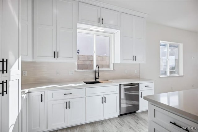 kitchen featuring white cabinets, backsplash, a sink, light countertops, and stainless steel dishwasher