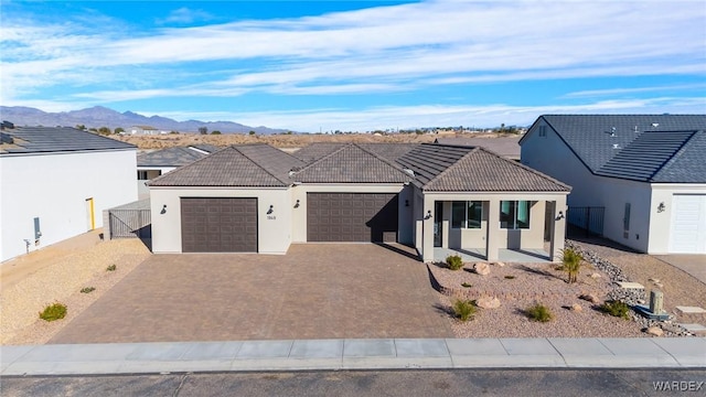 ranch-style home with an attached garage, a mountain view, a tiled roof, decorative driveway, and stucco siding