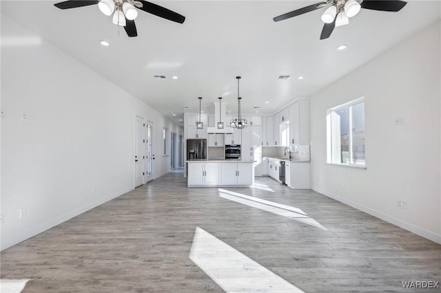 unfurnished living room featuring light wood-type flooring, a sink, baseboards, and recessed lighting