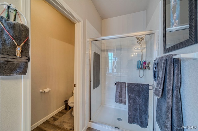 bathroom with a stall shower, wood finished floors, toilet, and baseboards