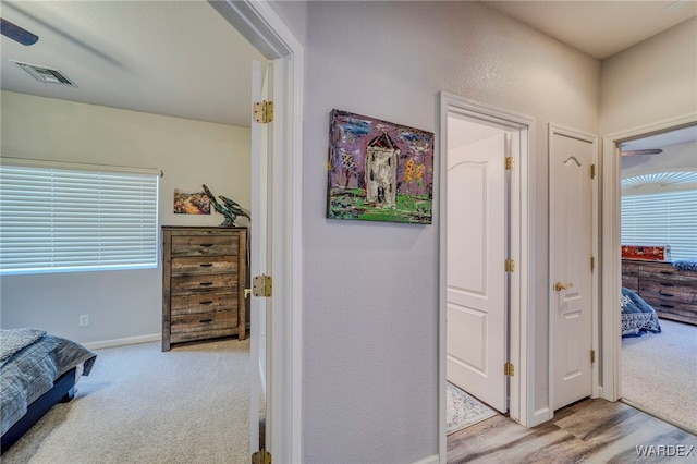 hall featuring baseboards, visible vents, and light colored carpet