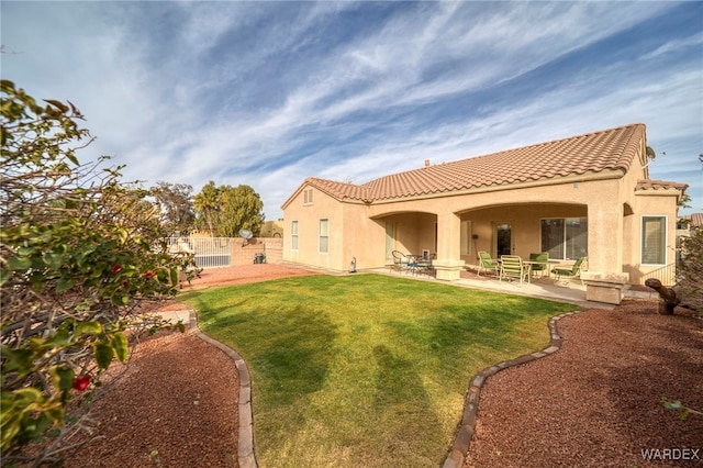 rear view of property featuring a tile roof, a patio, a lawn, and stucco siding