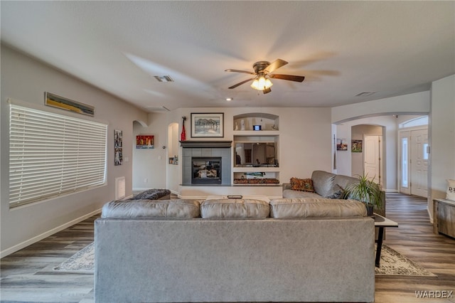 living area featuring visible vents, a tiled fireplace, arched walkways, and wood finished floors