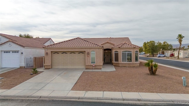 mediterranean / spanish house with driveway, a tiled roof, an attached garage, and stucco siding