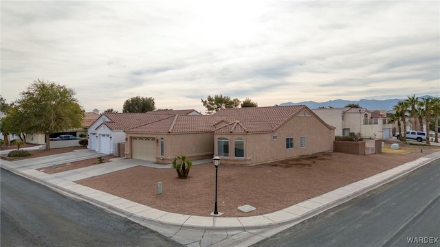 view of front of house with stucco siding, a mountain view, a garage, driveway, and a tiled roof