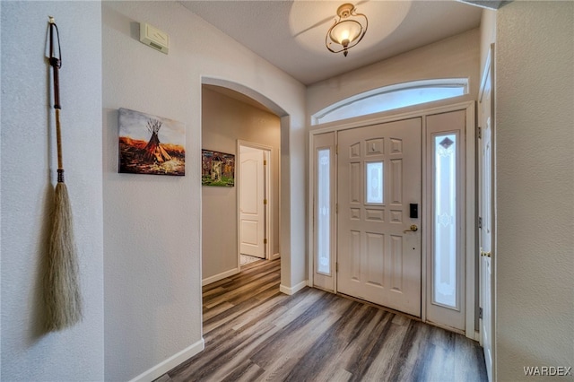 foyer entrance with baseboards, arched walkways, and dark wood-style flooring