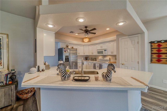 kitchen featuring white appliances, white cabinets, ceiling fan, a peninsula, and a sink