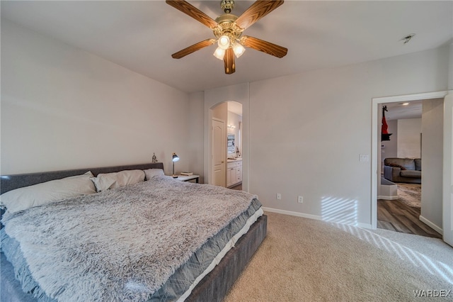 bedroom with arched walkways, ensuite bathroom, a ceiling fan, carpet flooring, and baseboards