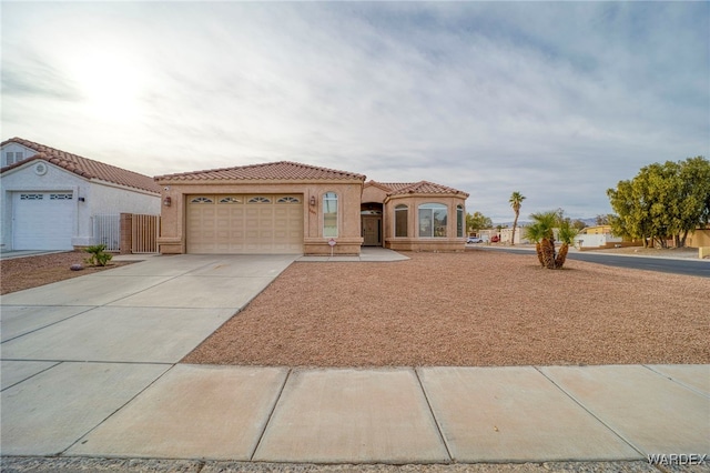 mediterranean / spanish-style home featuring a garage, concrete driveway, a tiled roof, and stucco siding