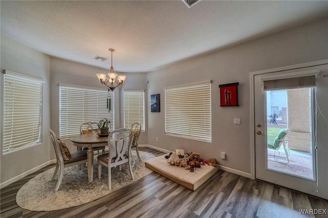 dining area with dark wood-style floors, baseboards, visible vents, and an inviting chandelier