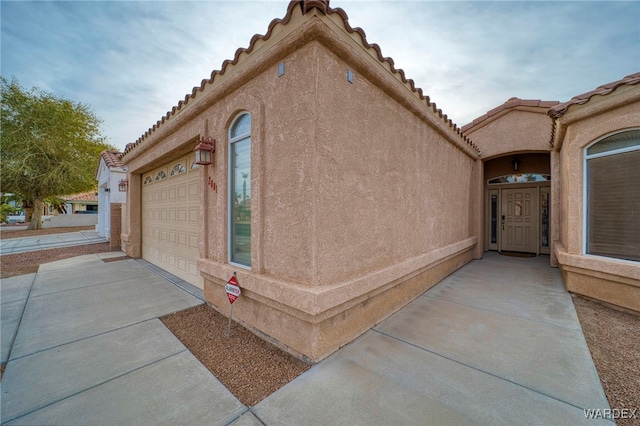 view of side of home featuring a garage, concrete driveway, and stucco siding