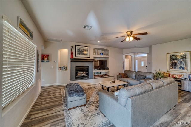 living area with arched walkways, visible vents, a tiled fireplace, wood finished floors, and baseboards