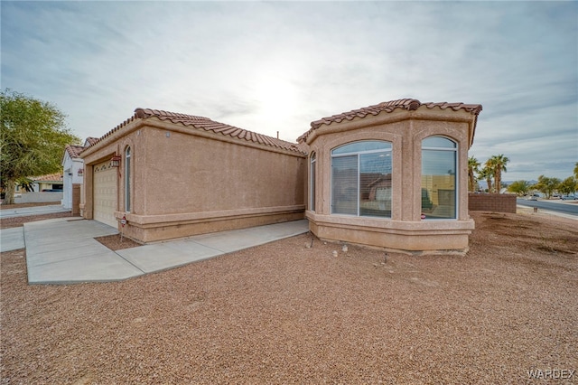 view of side of home featuring a garage, a tile roof, and stucco siding