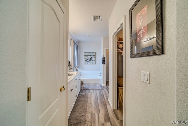 corridor with light wood-type flooring, visible vents, and a textured wall