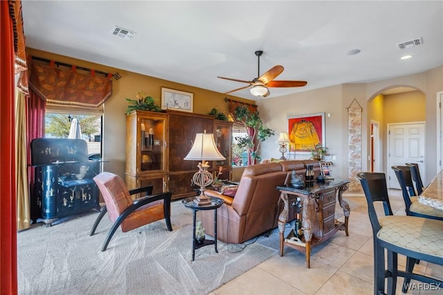 living room with arched walkways, light tile patterned flooring, visible vents, and a ceiling fan