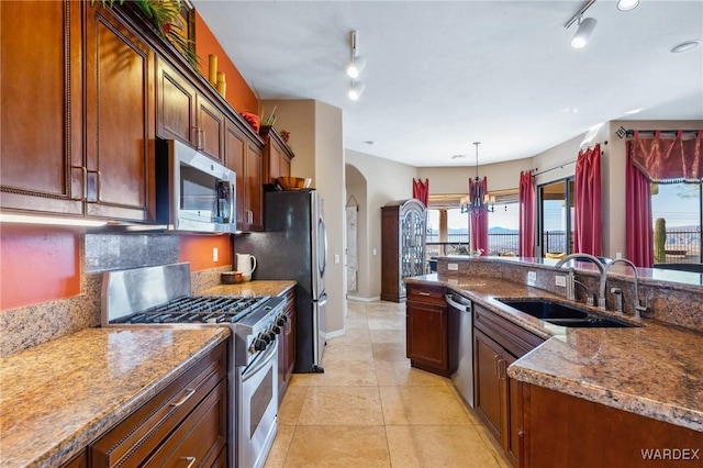 kitchen with arched walkways, pendant lighting, stainless steel appliances, a sink, and dark stone countertops