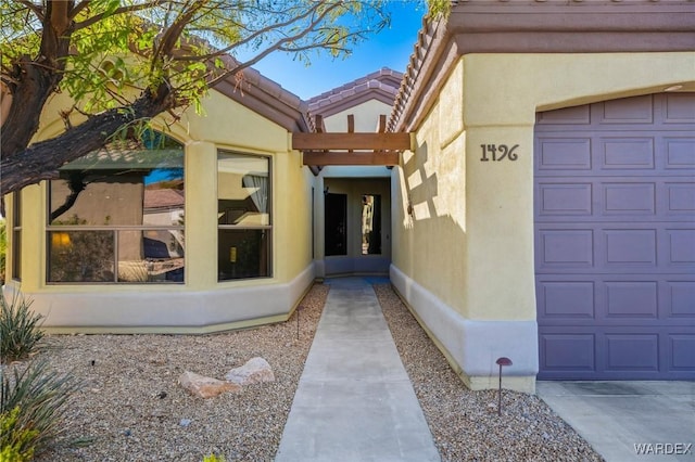 view of exterior entry featuring a tile roof, an attached garage, and stucco siding