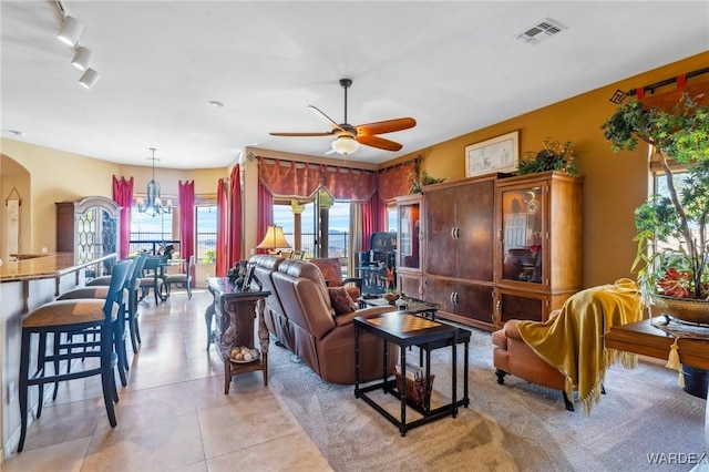 living area featuring light tile patterned floors, visible vents, arched walkways, and ceiling fan with notable chandelier