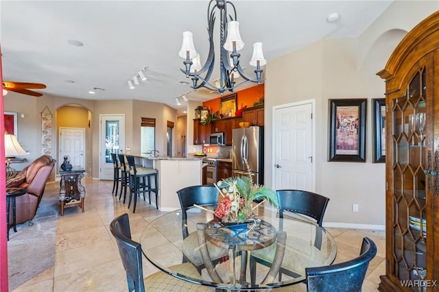 dining space with arched walkways, light tile patterned floors, rail lighting, baseboards, and ceiling fan with notable chandelier