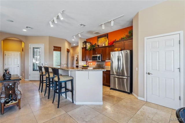 kitchen featuring a center island with sink, arched walkways, light stone counters, a kitchen breakfast bar, and stainless steel appliances