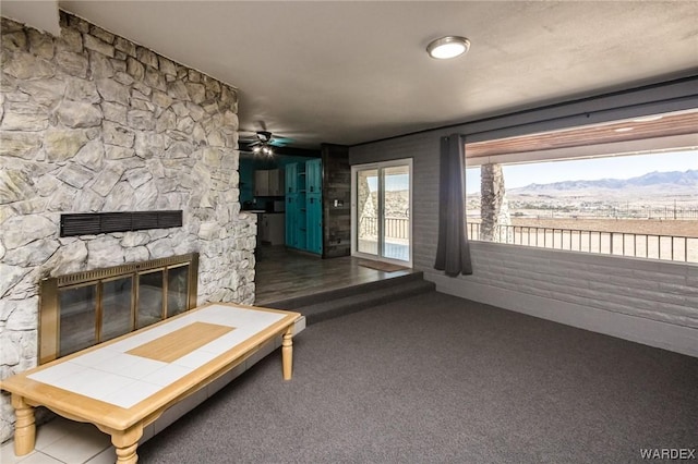 unfurnished living room with ceiling fan, a mountain view, a fireplace, visible vents, and dark carpet