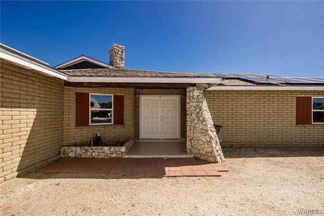 entrance to property with solar panels, brick siding, and a chimney