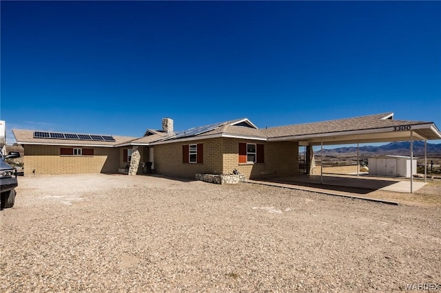 rear view of property with a storage shed, solar panels, brick siding, an outdoor structure, and a chimney