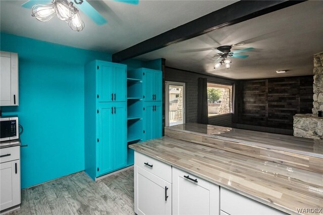 kitchen with a ceiling fan, white cabinets, beamed ceiling, open shelves, and stainless steel microwave