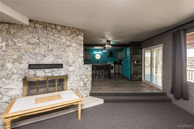 unfurnished living room with dark carpet, a stone fireplace, and ceiling fan