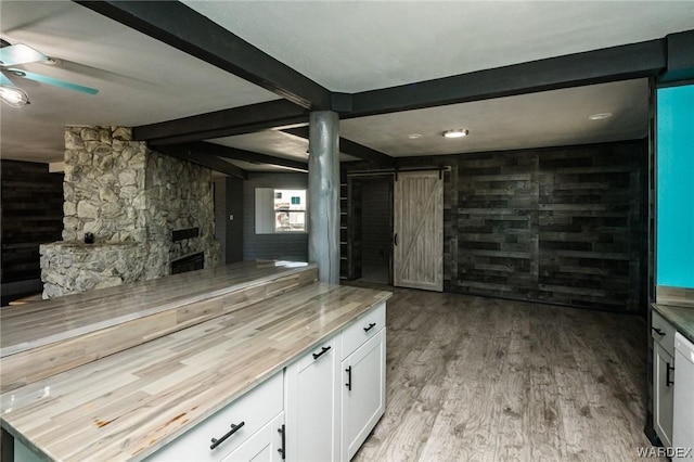 interior space with a barn door, a fireplace, white cabinetry, beam ceiling, and light wood finished floors