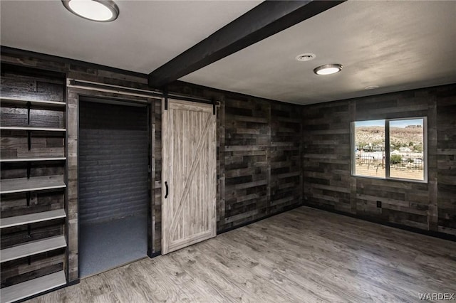 unfurnished room featuring wood finished floors, wooden walls, beam ceiling, and a barn door